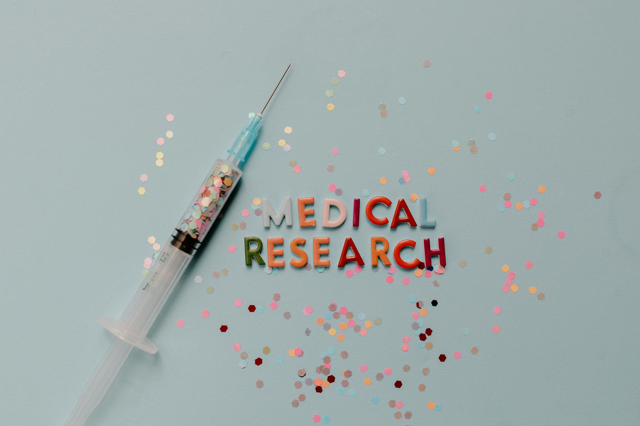 Close-up of a syringe with colorful confetti on medical research theme.